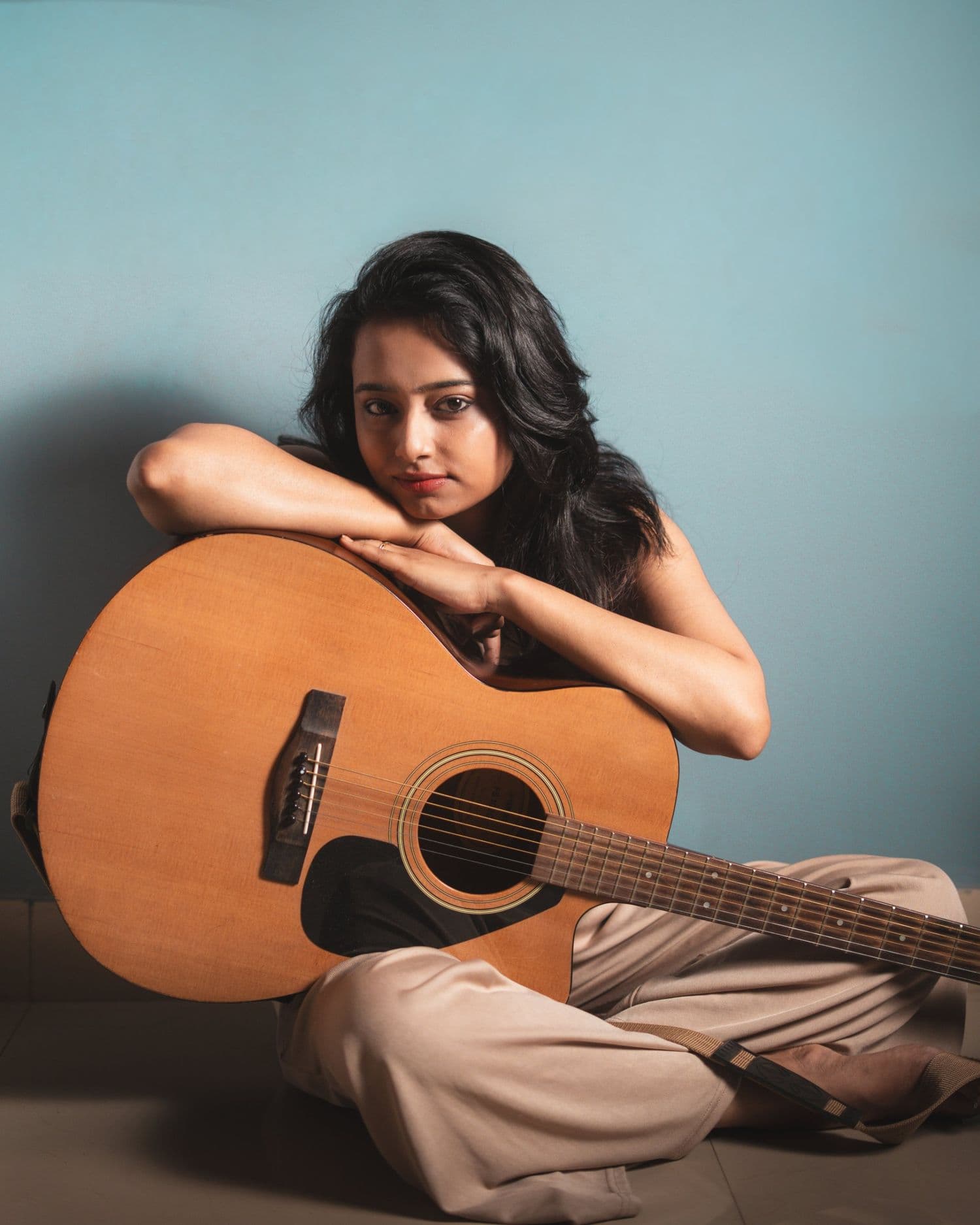 Ankita Barwad sitting cross-legged on the floor with an acoustic guitar, resting her chin on her arms.