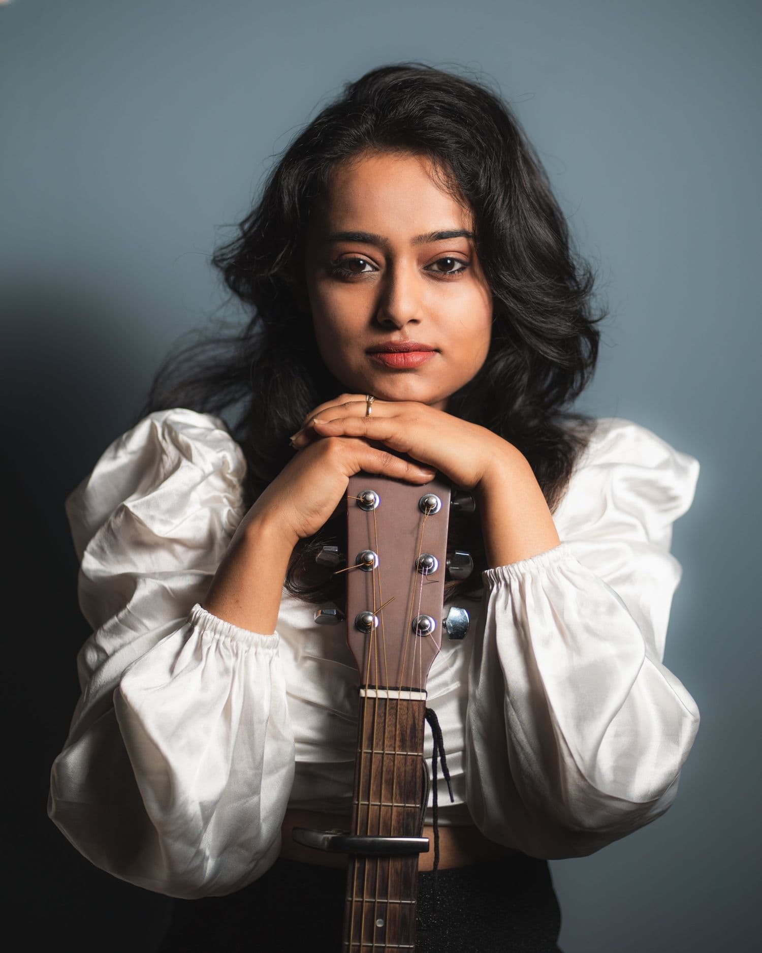 Ankita Barwad in a white puff-sleeve blouse, resting her chin on her hands on the headstock of an acoustic guitar.